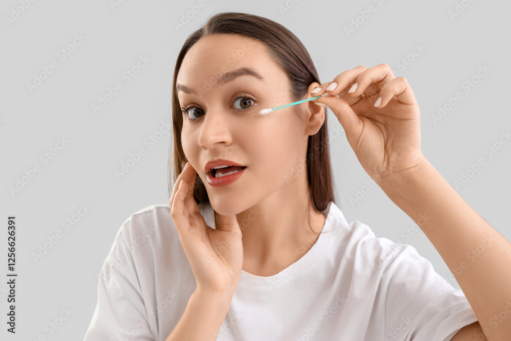 Young woman cleaning face with cotton bud on light background, closeup Young woman cleaning face with cotton bud on light background, closeup