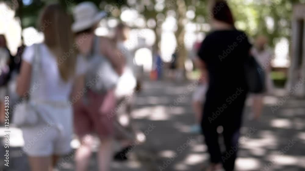 Blurred group of people walking in a city park, with dappled sunlight filtering through the trees. Perfect background for projects related to urban life, travel, or leisure.