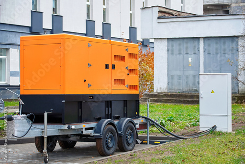 Obraz na płótnie Industrial diesel generator connected to power distribution box. Backup generator on trailer supplying emergency power, industrial energy solutions and temporary electricity distribution. w salonie