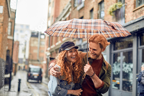 Young couple taking a selfie while under an umbrella avoiding rain photo