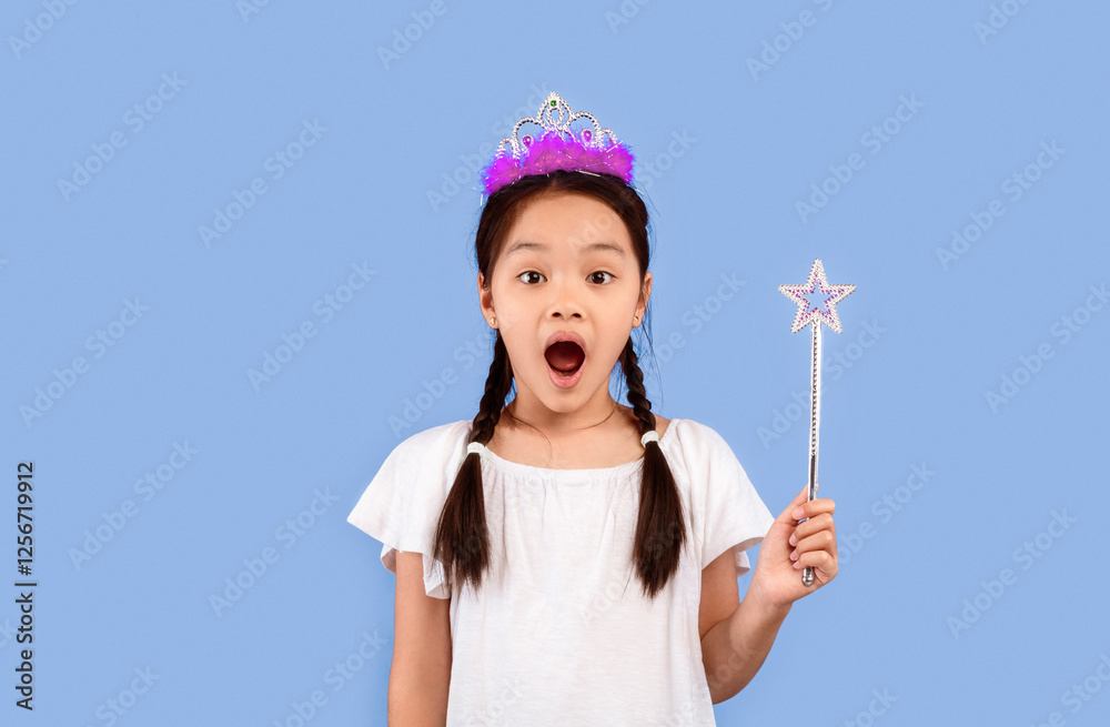 Surprised Little Asian Girl Holding Magic Stick Wearing Crown Posing Over Purple Background. Studio Shot Surprised Little Asian Girl Holding Magic Stick Wearing Crown Posing Over Purple Background. Studio Shot