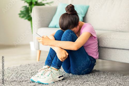 Принти на полотні Depressed Indian teen girl with cellphone crying on floor at home, suffering from cyber bullying, being harassed online