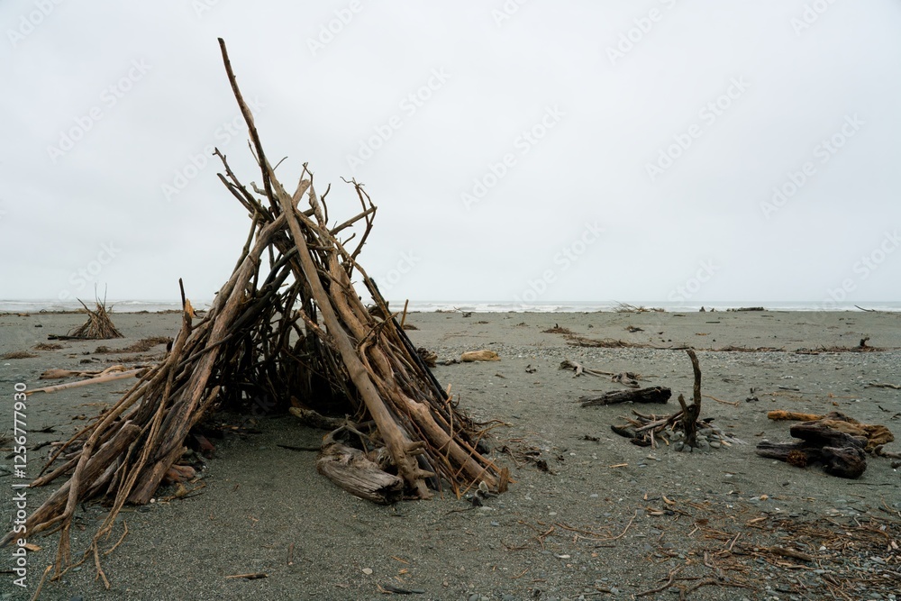 Shelter on the Beach Made from Driftwood on a Grey Day – Secluded Coastal Scene Shelter on the Beach Made from Driftwood on a Grey Day – Secluded Coastal Scene