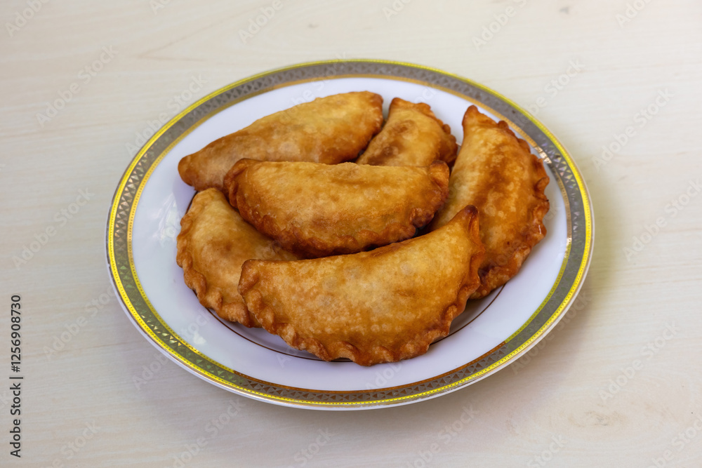 Delicious Chicken Puli Pitha, fried and served on a white plate on a wooden backdrop. This popular traditional cake in Bangladesh is also made with vegetable, fish, meat, coconut, and jaggery fillings Delicious Chicken Puli Pitha, fried and served on a white plate on a wooden backdrop. This popular traditional cake in Bangladesh is also made with vegetable, fish, meat, coconut, and jaggery fillings