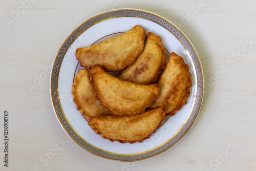 Yummy Chicken Puli Pitha, fried and served on a white plate on a wooden backdrop. It is popular traditional cake in Bangladesh is also made with vegetable, fish, meat, coconut, and jaggery fillings photo