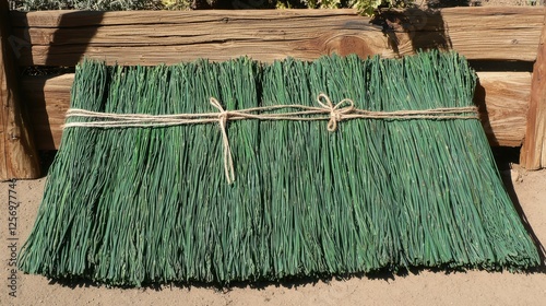 Bundled green grass mat resting on the ground near wooden structure in a natural setting