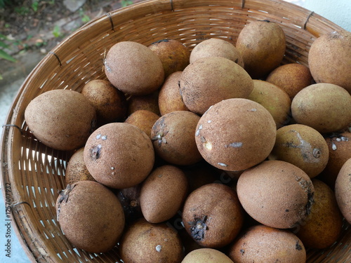 Group of Sapodilla fruits (Manilkara zapota) in brown basket. Tropical fruit in market, Thailand photo