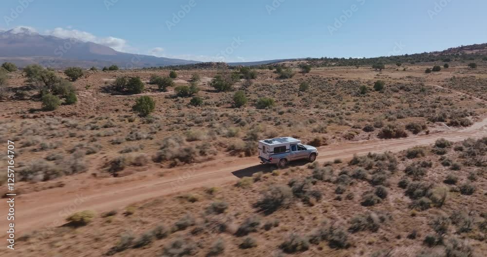 Aerial view following truck with camper down dusty remote desert dirt road Aerial view following truck with camper down dusty remote desert dirt road