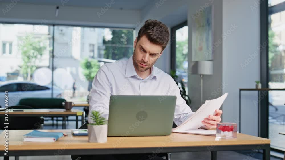 Busy employee reviewing papers at modern coworking space closeup. Frowned man Busy employee reviewing papers at modern coworking space closeup. Frowned man