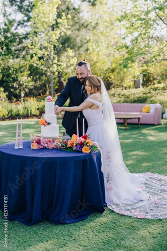 A joyful couple celebrates their love during a wedding cake cutting ceremony in a beautifully decorated garden, surrounded by loved ones and vibrant flowers, creating unforgettable memories for all