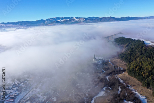 Aerial view of foggy misty mountain village and church tower at winter photo