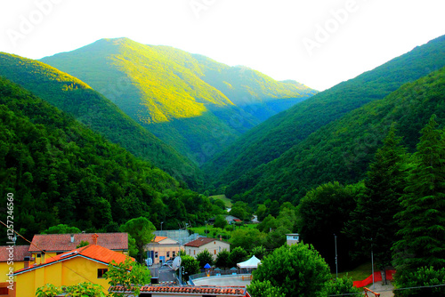Mystical view from Sefro (Macerata) with the Sibillini Mountains standing majestic in the background, partly lit by the late afternoon sunlight, covered by vegetation, and buildings in the foreground