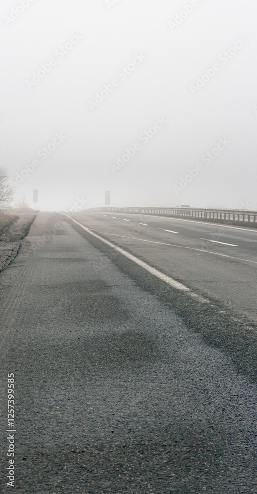 Empty highway in the fog. Bad weather on the road. Road on foggy day in perspective with copy space. Driving conditions concept. Ghostly misty road. Caution and danger on the road. Moody weather