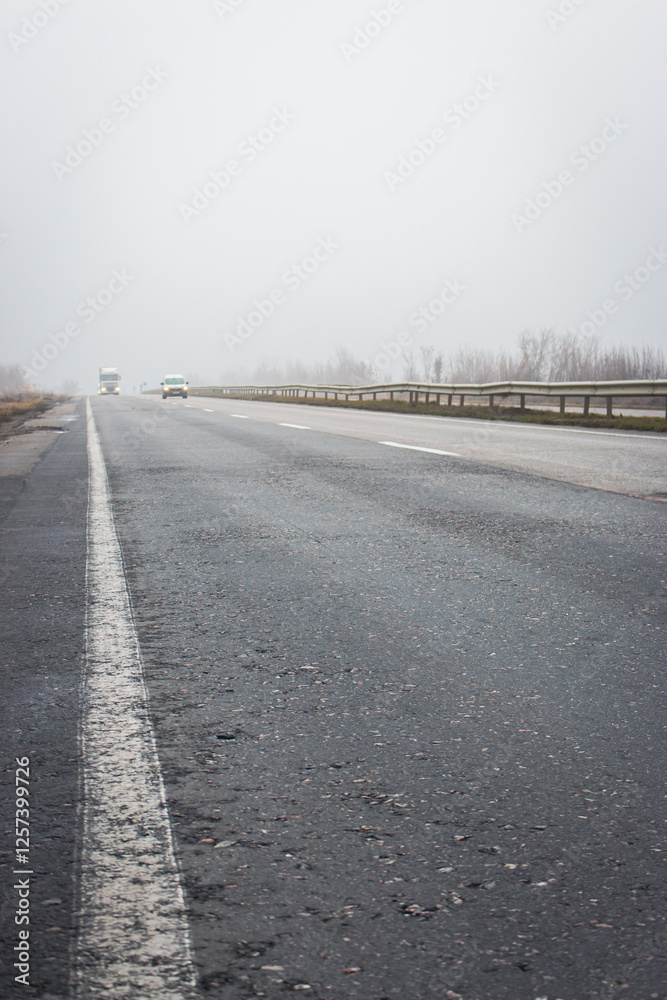 Cars on highway in the fog. Bad weather on the road. Road on foggy day in perspective with copy space. Driving conditions concept. Ghostly misty road. Caution and danger on the road.