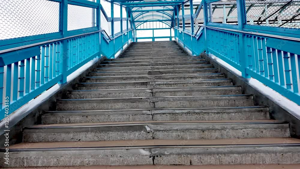 Climbing up concrete stairs with blue railings in a covered walkway, showcasing the journey of ascension and urban design. slow motion Climbing up concrete stairs with blue railings in a covered walkway, showcasing the journey of ascension and urban design. slow motion
