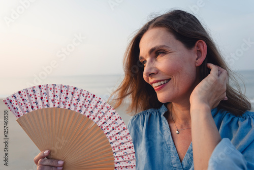 Beautiful woman holding hand fan under clear sky at beach