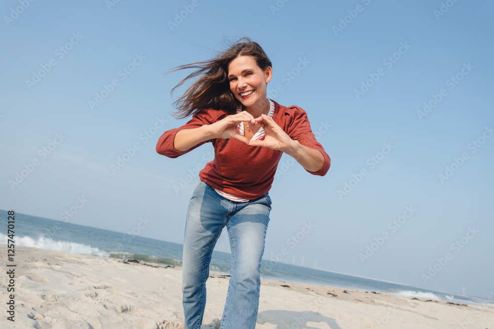 Smiling woman making heart shape with hand at beach Smiling woman making heart shape with hand at beach