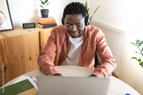 Focused young man working from home using laptop and headphones