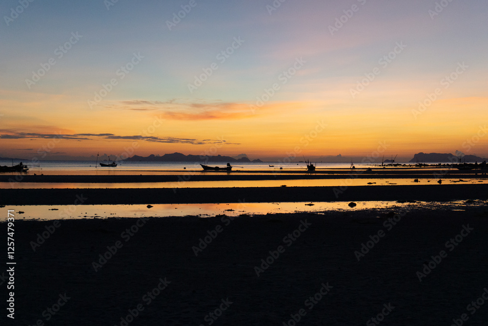 Obraz premium Stunning sunset over a tranquil beach with silhouetted fishing boats and distant islands.