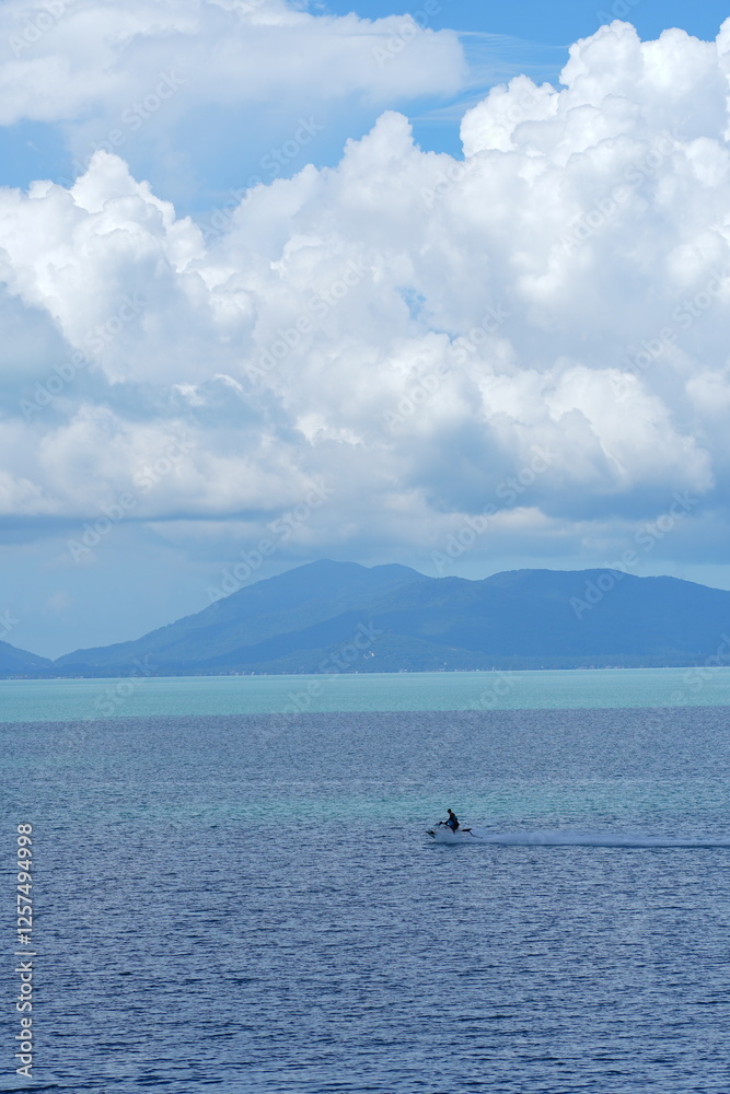 Serene tropical seascape with mountains under a bright blue sky and fluffy white clouds Serene tropical seascape with mountains under a bright blue sky and fluffy white clouds