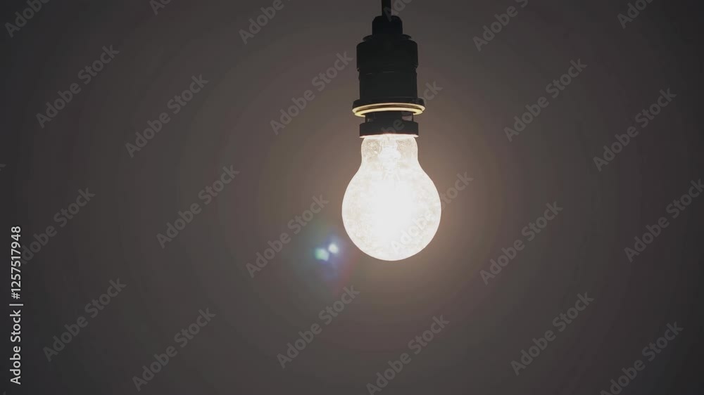 A dimly lit video frame featuring a glowing light bulb hanging from above, captured from a low angle against a dark, minimalist background. A dimly lit video frame featuring a glowing light bulb hanging from above, captured from a low angle against a dark, minimalist background.