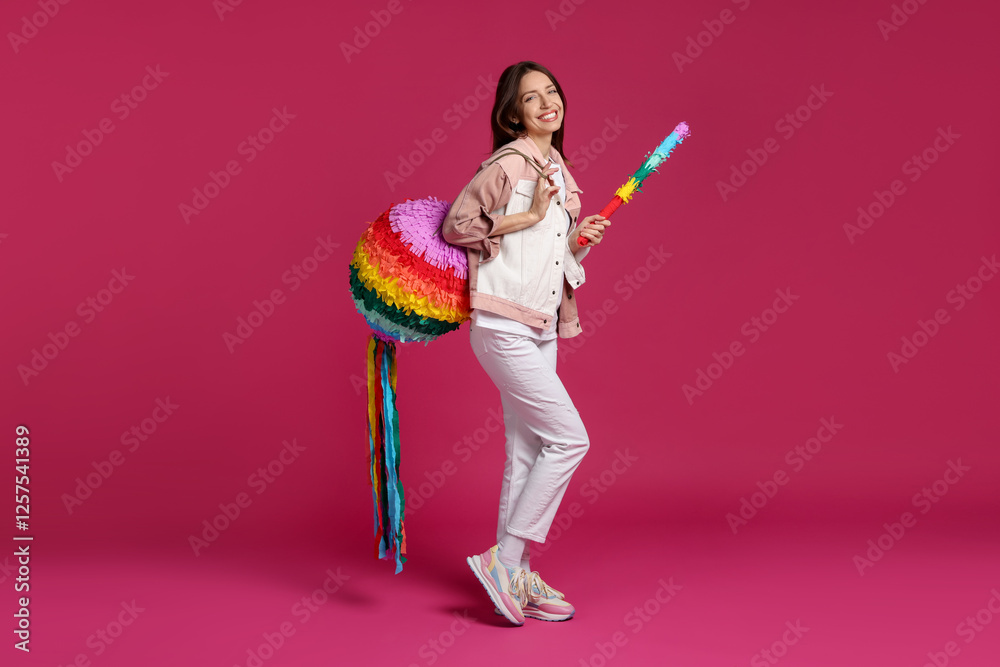 Happy woman with colorful pinata and stick on pink background Happy woman with colorful pinata and stick on pink background