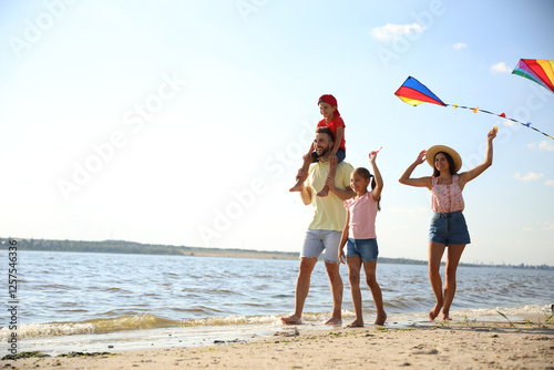 Happy parents and their children playing with kites on beach near sea. Spending time in nature