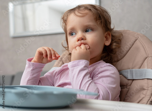 Obraz na plátně A thoughtful toddler focused on self-feeding while chewing a piece of sausage