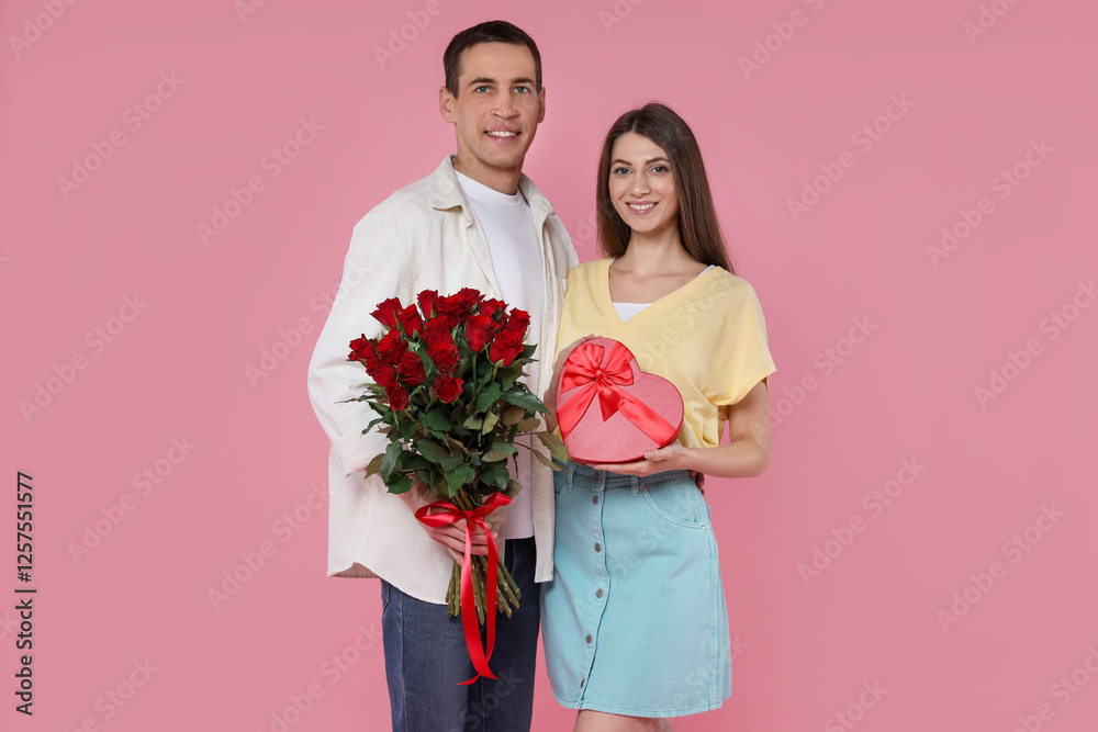 Lovely couple with bouquet of red roses and gift box on pink background. Valentine's day celebration Lovely couple with bouquet of red roses and gift box on pink background. Valentine's day celebration