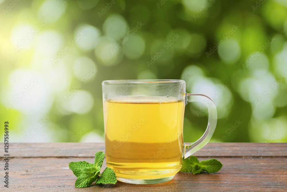 Aromatic mint tea in glass cup and fresh leaves on wooden table outdoors Aromatic mint tea in glass cup and fresh leaves on wooden table outdoors