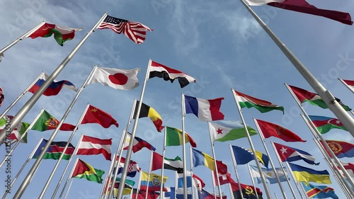 A collection of international flags waving on tall poles against a bright blue sky, symbolizing global unity and diversity.