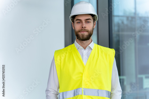 Young male engineer in a yellow vest and protective cap looking determined