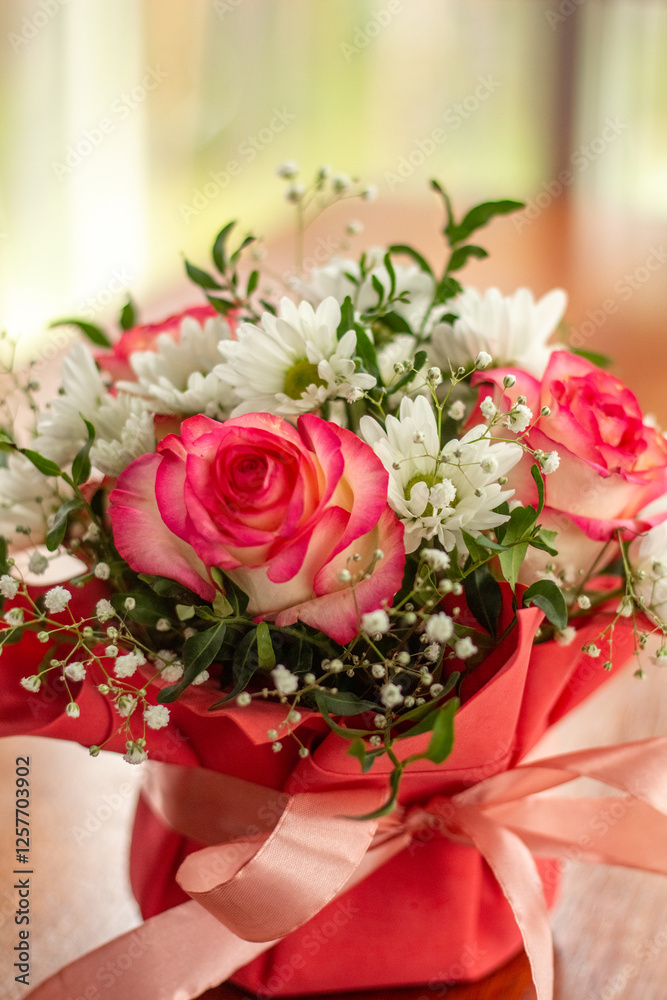 Obraz premium Closeup a Beautiful bouquet of flowers in a red box on a wooden table against light window at restaurant. Gift for holiday, birthday, Wedding, Mother's Day, Valentine's day, Women's Day. 