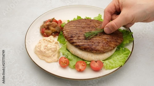 Serbian pljeskavica served on pita with traditional Balkan side dishes. Delicious Balkan style burger pljeskavica grilled meat patty decorated with rosemary