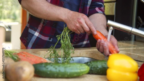 A close-up view of a person washing fresh vegetables under running water in a modern kitchen. The scene highlights healthy eating, food preparation, and hygiene. Colorful bell peppers, cucumbers
