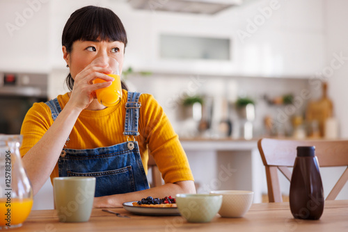 Woman drinking fresh orange juice while relaxing and having breakfast at home
