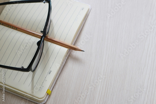 Photography pencil and notepad with eyeglasses over white table view from above