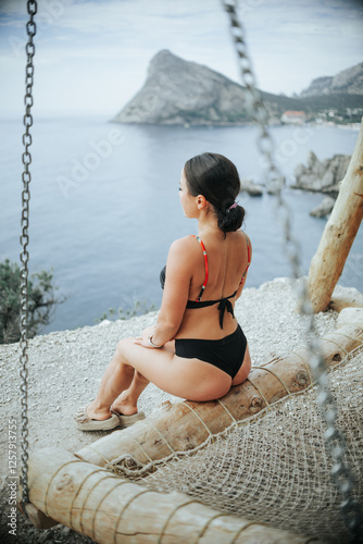 Beautiful girl with glasses bathing on a swing, over a cliff overlooking the sea and mountains