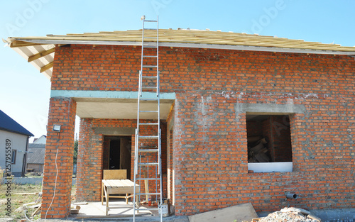 An aluminum extension ladder is attached to a house being built of brick during roofing construction.