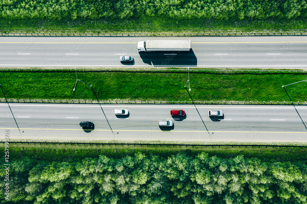 Aerial drone view of highway asphalt road with cars and trucks driving through green summer woods. Cargo delivery logistic concept