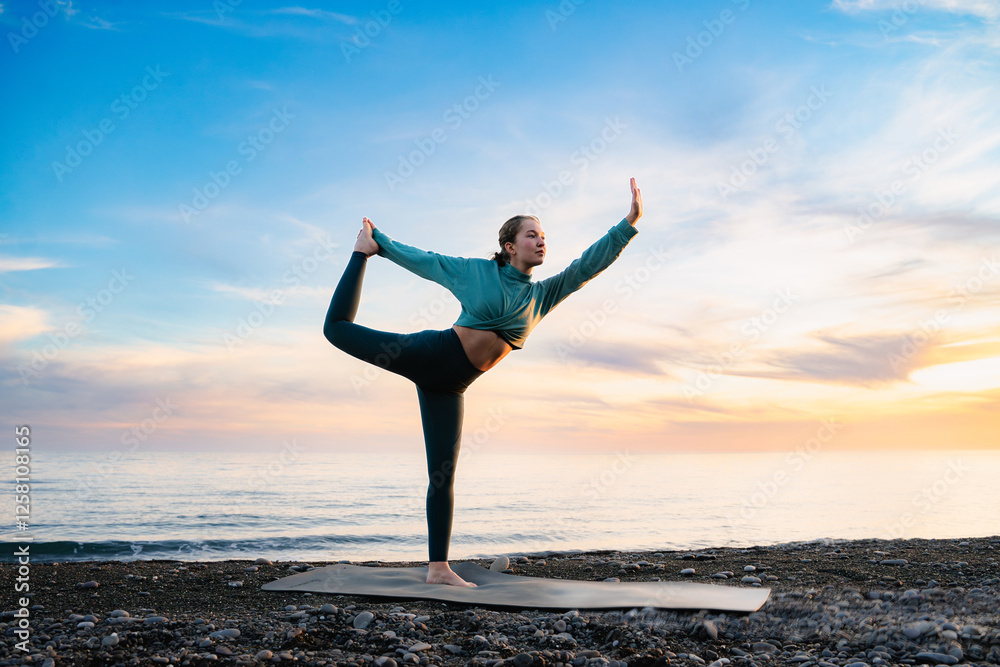 Woman practicing yoga king dancer pose or natarajasana to standing balance on a stone beach at sunset or sunrise. Back-bending asana exercise. Exercise, fitness, stretching, workout, pilates outdoors. Woman practicing yoga king dancer pose or natarajasana to standing balance on a stone beach at sunset or sunrise. Back-bending asana exercise. Exercise, fitness, stretching, workout, pilates outdoors.