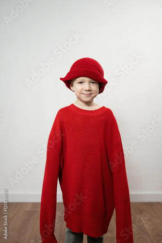 Child in oversized red sweater and hat with playful expression photo