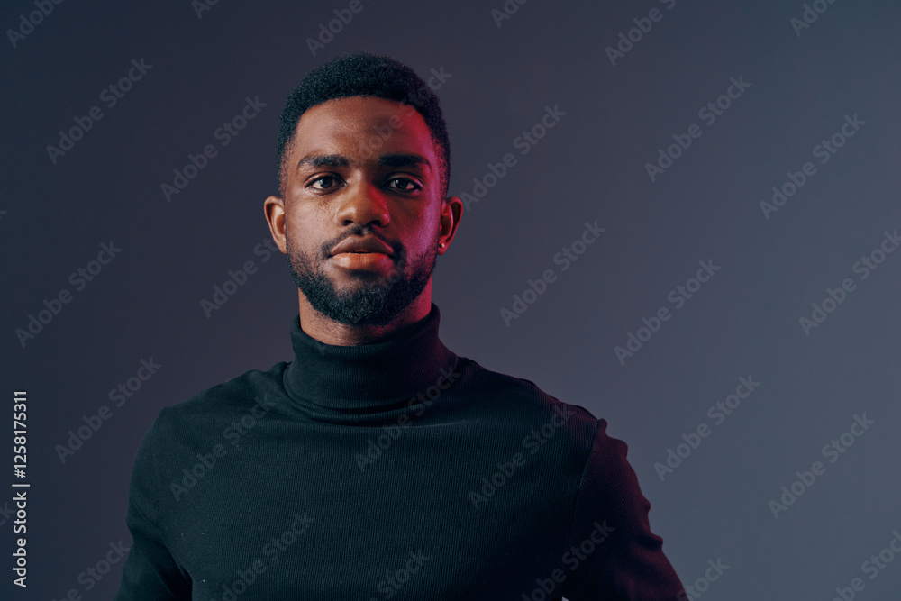 Obraz premium Portrait of a serious African male model in a black turtleneck sweater against a gradient grey background, conveying confidence and style, ideal for fashion and lifestyle concepts