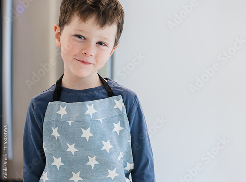 Child smiling in a star patterned apron in bright kitchen photo