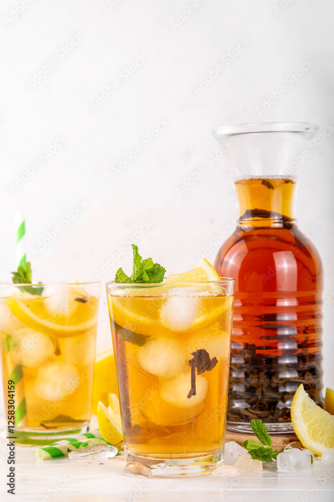 Iced tea cocktail drink, cold summer drink with black tea, lemon, mint and crushed ice, tasty refreshing non-alcohol mocktail on white wooden table background Iced tea cocktail drink, cold summer drink with black tea, lemon, mint and crushed ice, tasty refreshing non-alcohol mocktail on white wooden table background