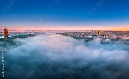 Obraz na płótnie Thick fog covering Riga city in colorful sunrise colors. Drone view over old town, TV tower and river Daugava. Twilight colors in misty weather. w salonie