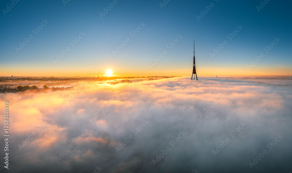 Thick fog covering Riga city in colorful sunrise colors. Drone view over old town, TV tower and river Daugava. Twilight colors in misty weather.