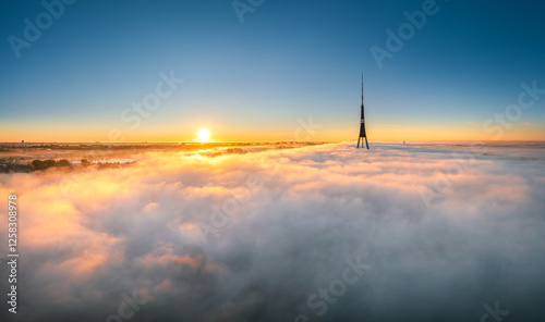 Obraz na płótnie Thick fog covering Riga city in colorful sunrise colors. Drone view over old town, TV tower and river Daugava. Twilight colors in misty weather. w salonie