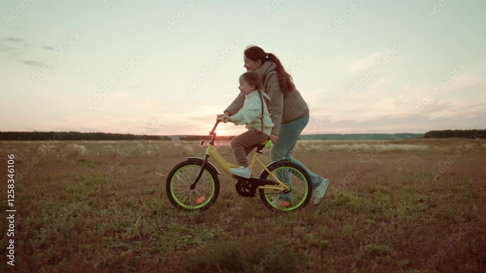 Happy family, mother teaches to ride child girl daughter double calf bike, kids cycling sunset, child with female parent learning ride bike park sunset, kids games field, happy family concept Happy family, mother teaches to ride child girl daughter double calf bike, kids cycling sunset, child with female parent learning ride bike park sunset, kids games field, happy family concept