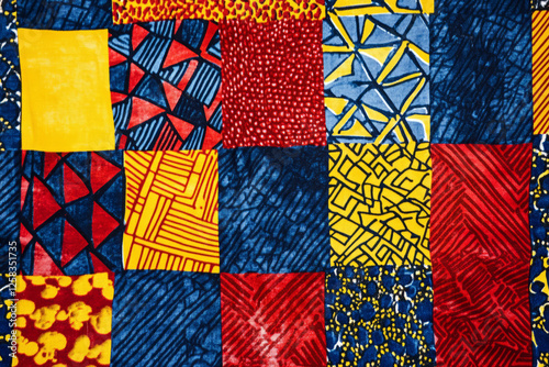Bright African wax print textile, bold geometric patterns in red, yellow, and deep blue, creating rich cultural texture.